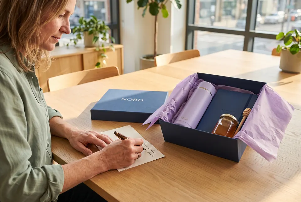 Eine Mitarbeiterin packt eine Geschenkbox für einen Kunden und schreibt eine persönliche Karte dazu.