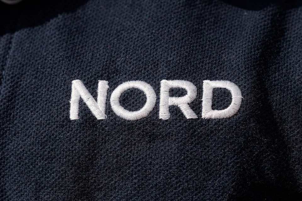 Nahaufnahme einer gestickten Wortmarke aus weißem Garn auf einem marineblauen Polo.